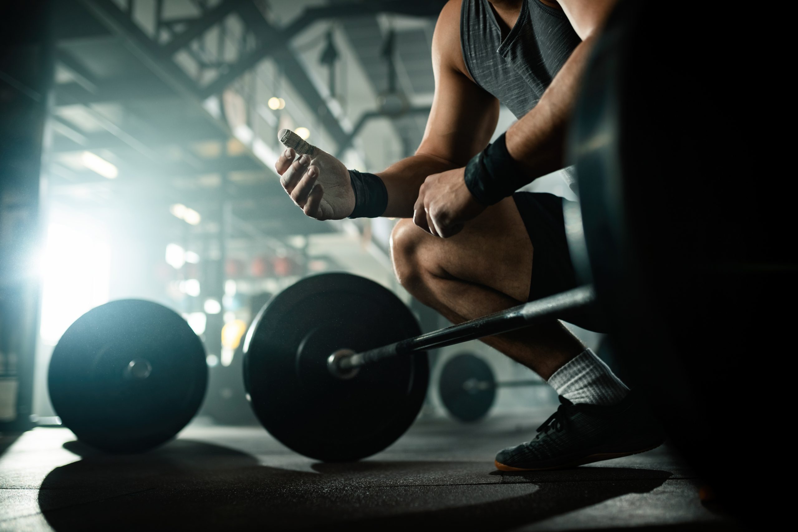 Low angle view of unrecognizable muscular build man preparing for lifting a barbell in a health club.